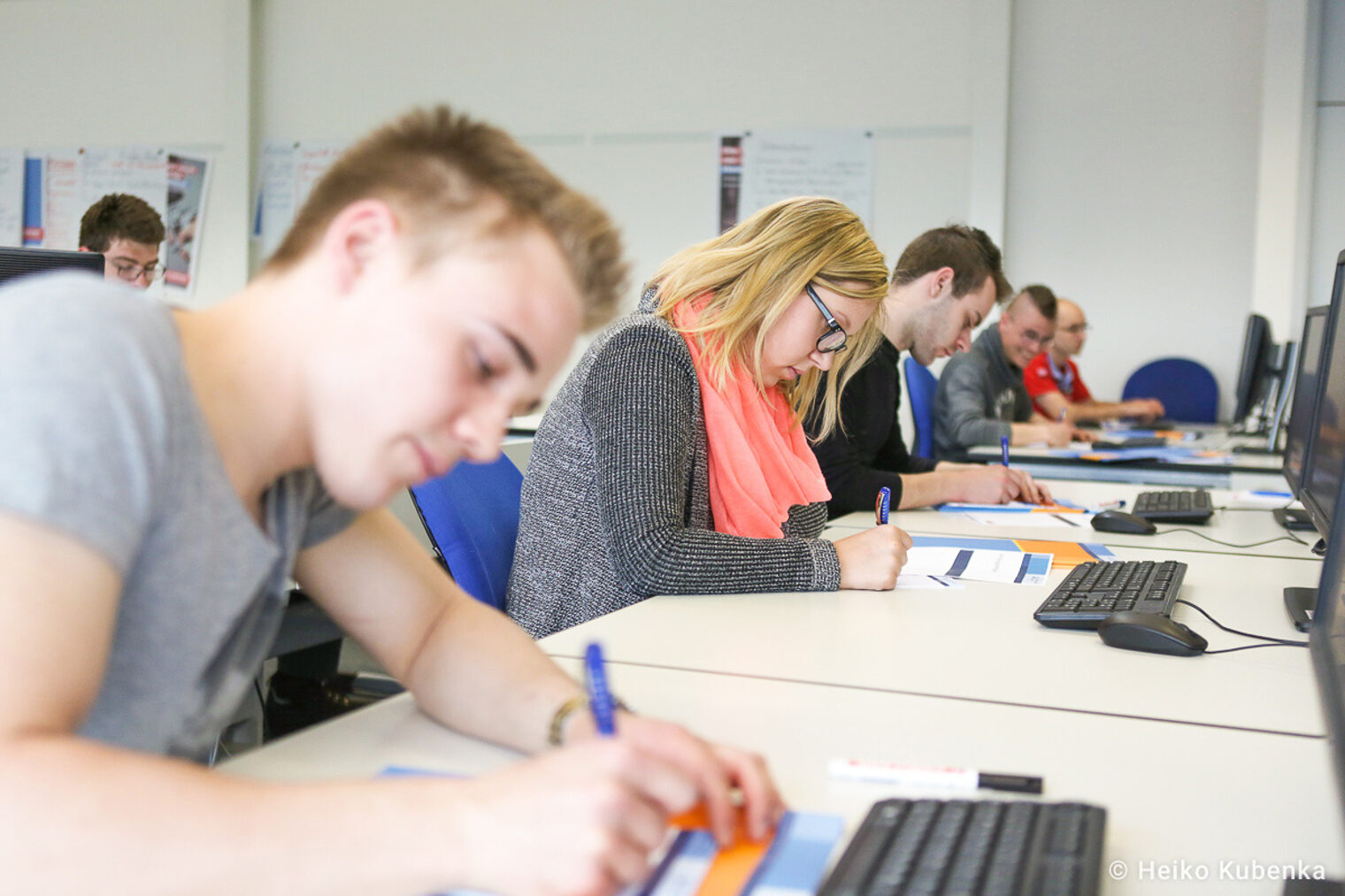 Unterrichtssituation - junge Teilnehmende schreiben auf Arbeitsblättern, während sie vor Computern sitzen