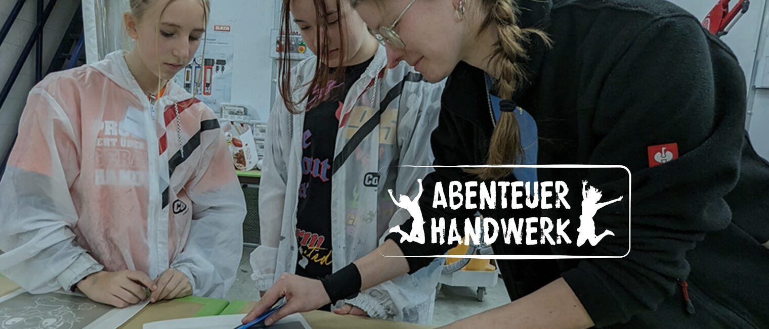 Ausbildungsmeisterin zeigt jungen Mädchen, wie sie eine Folie luftblasenfrei auf eine Scheibe anbringen.